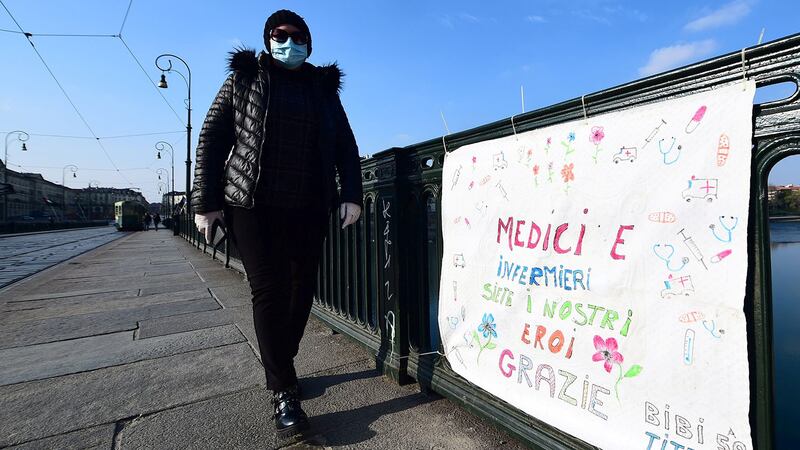 2020年3月13日,一名戴着口罩的妇女走到意大利罗马维托里奥·埃马努埃莱二世桥上的横幅上,上面写着“医生和护士是我们的英雄”。(路透社)