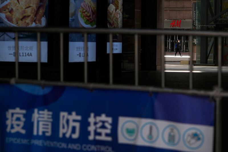 2022年5月1日,北京一名戴着口罩的妇女走过关闭的商场。(美联社)